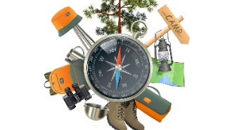 Compass surrounded by camping supplies, including lantern, boots, binoculars, backpack, among others