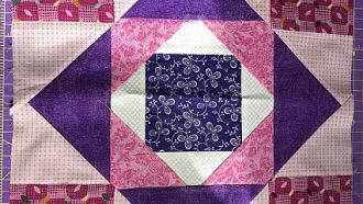 Handmade quilt in a Square within a square meets Cat's Cradle design. Various shades of pink, purple and white.